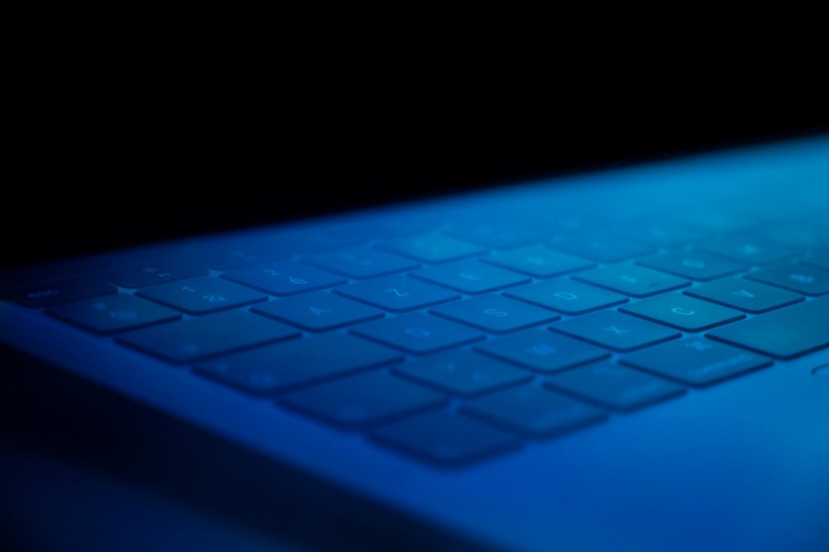 Laptop keyboard lit by cool blue light in a darkened room