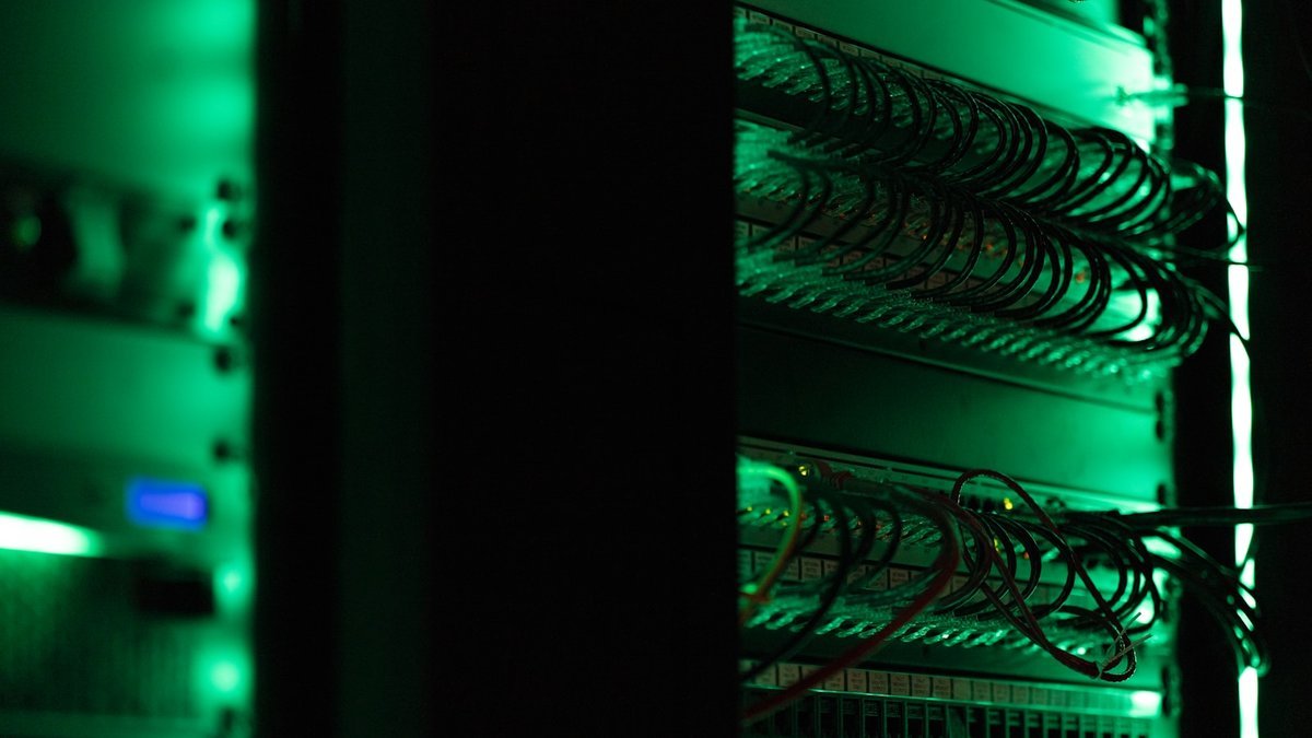 Server racks and patch cabling lit green in a dark on-premise server room