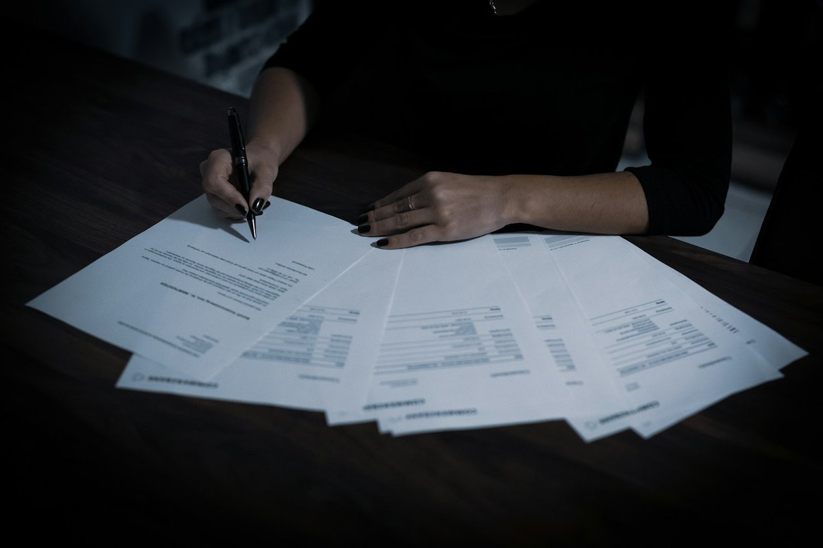 Person signing a fanned-out set of printed forms at a desk