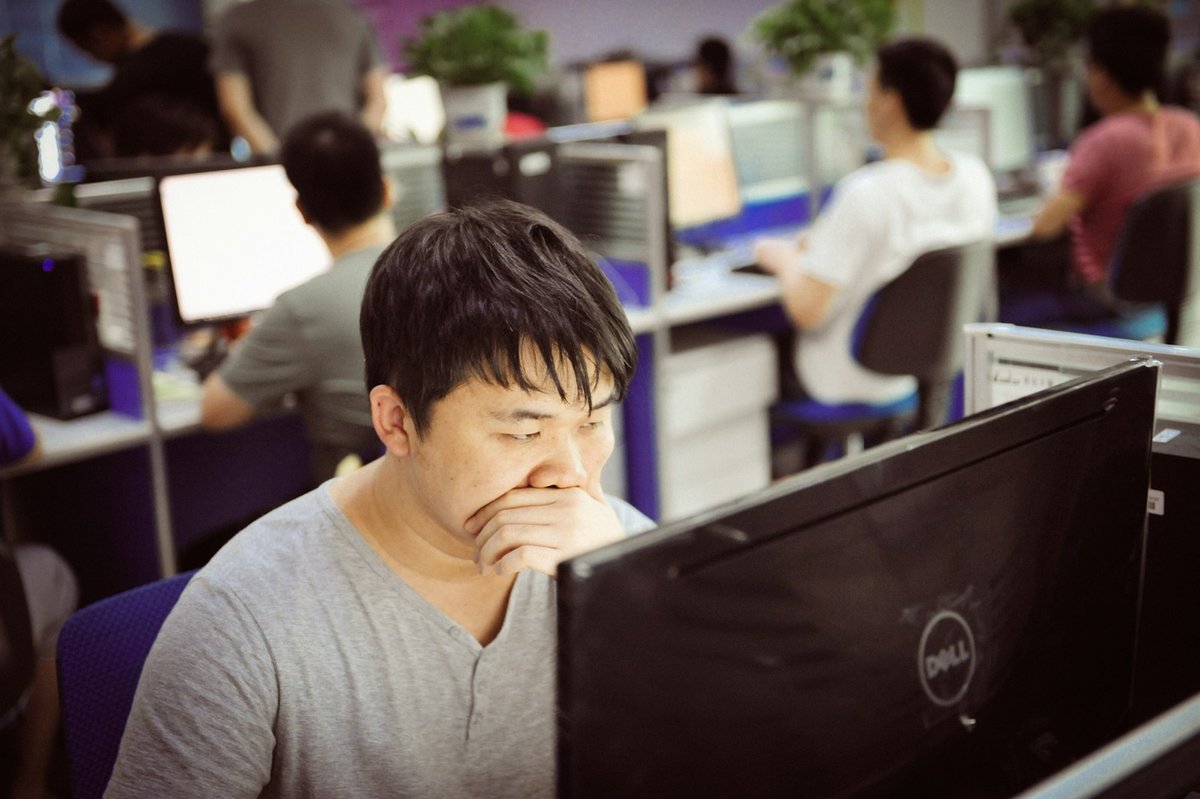 Office worker concentrating at a desktop computer in a busy open-plan office