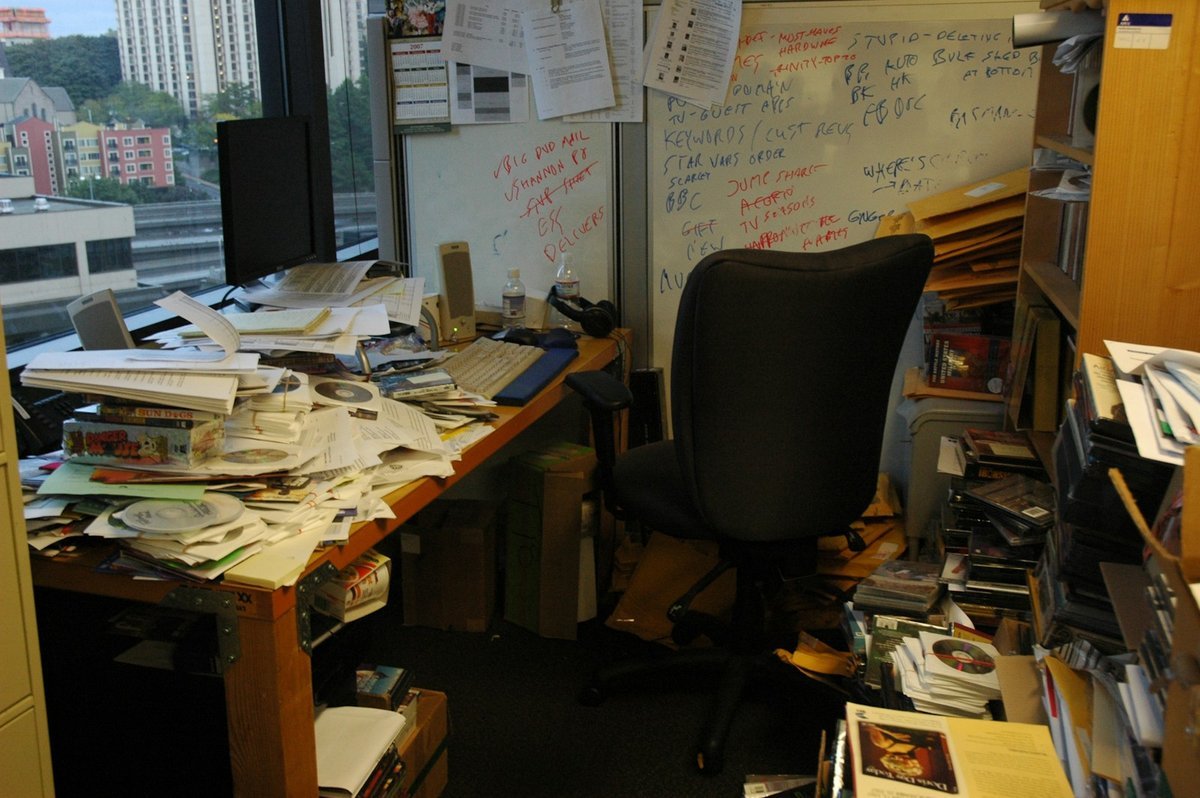 Office desk buried under stacks of paper files and printouts