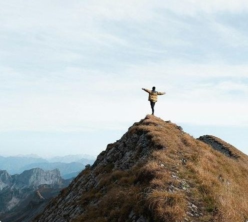 A person standing on a mountain peak with arms raised