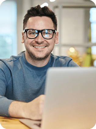 Smiling man in glasses working on a laptop.