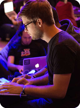 Man with glasses typing on a laptop at a tech event.