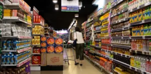 Shopper pushing cart through supermarket aisle.