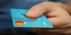 Hand offering a blue Mastercard debit card.