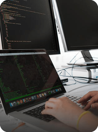 Hands coding on laptop with dual monitors.