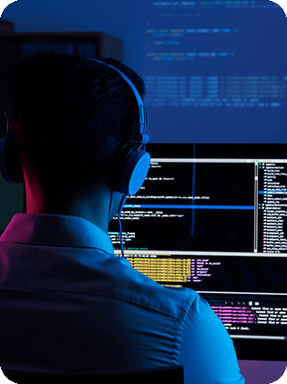 Programmer with headphones coding in front of monitors.