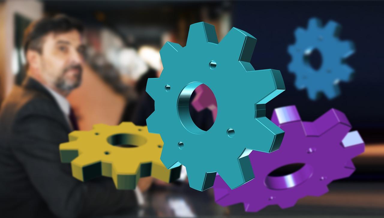Colorful gears floating over a blurry businessman.