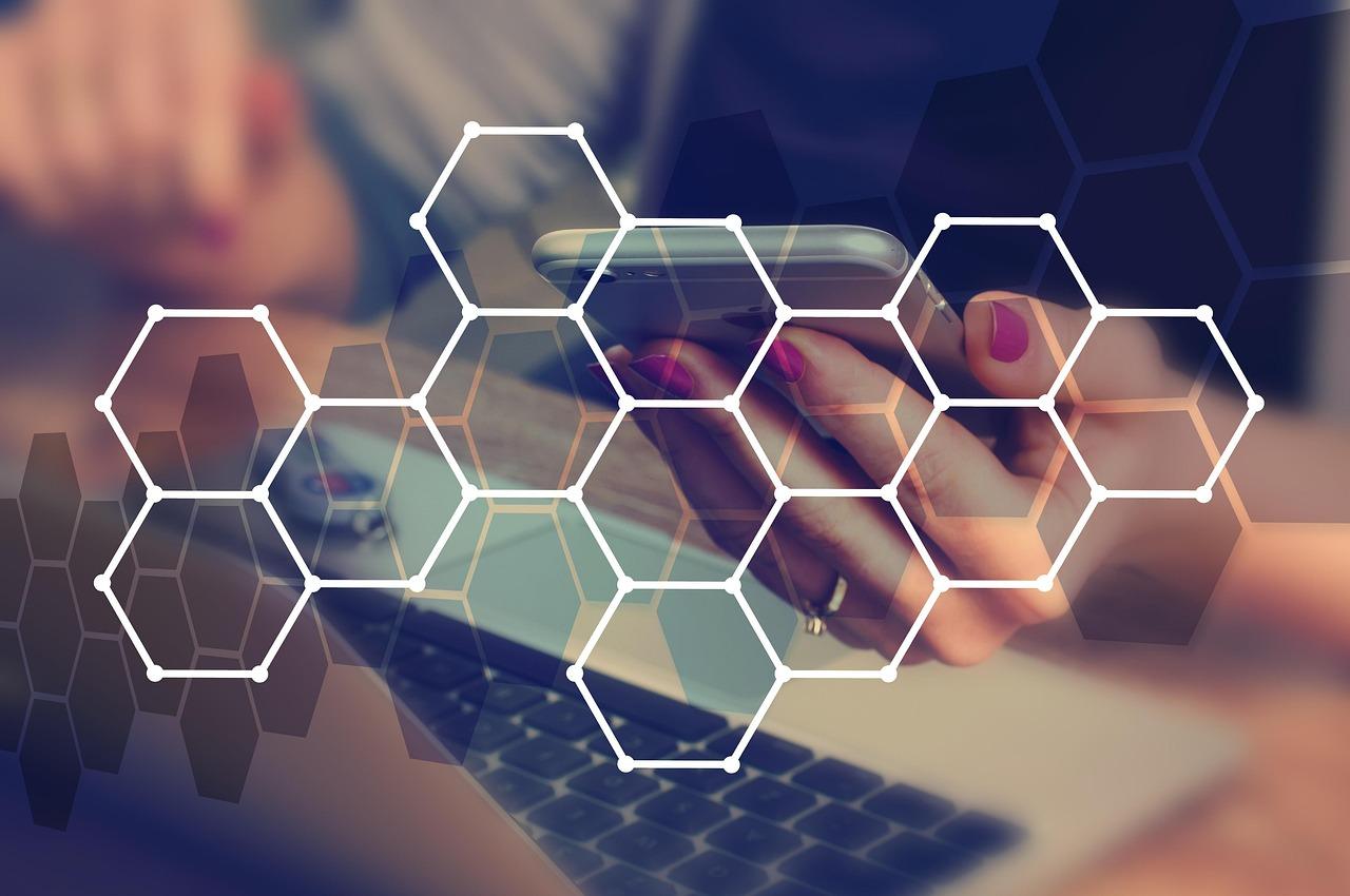 Hands operating smartphone and laptop with network hexagons.